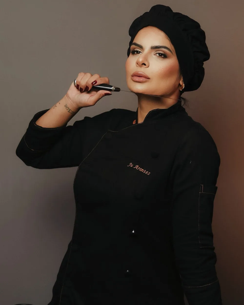 A chef Juliana Arantes de dólmã preta, com o nome bordado no peito.